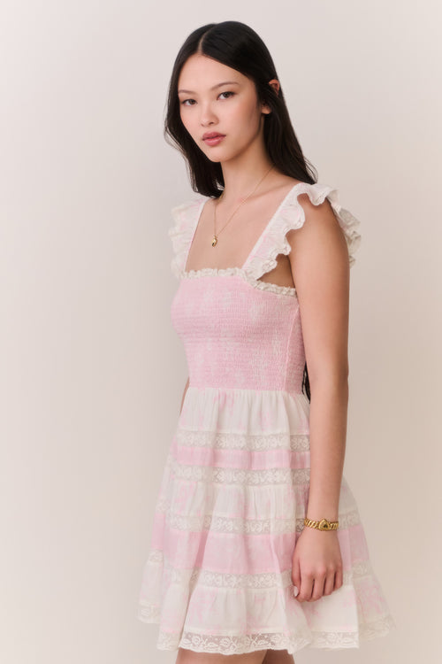 Woman wearing pink dress with lace details on a plain background