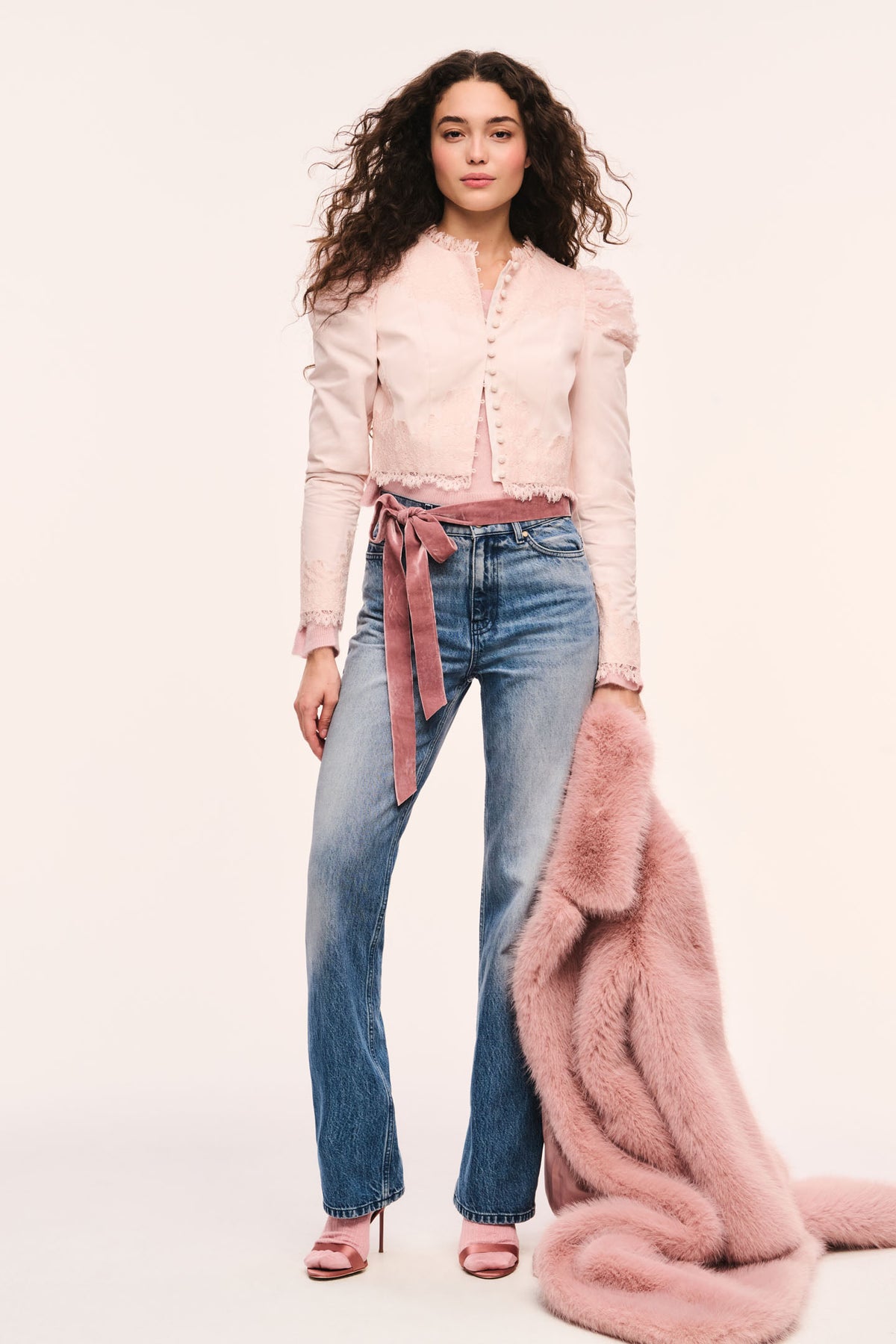 Light pink cropped jacket front view with button placket, puff sleeves, and lace-trim ruffle edges styled over a pink sweater and a pink fur coat with jeans