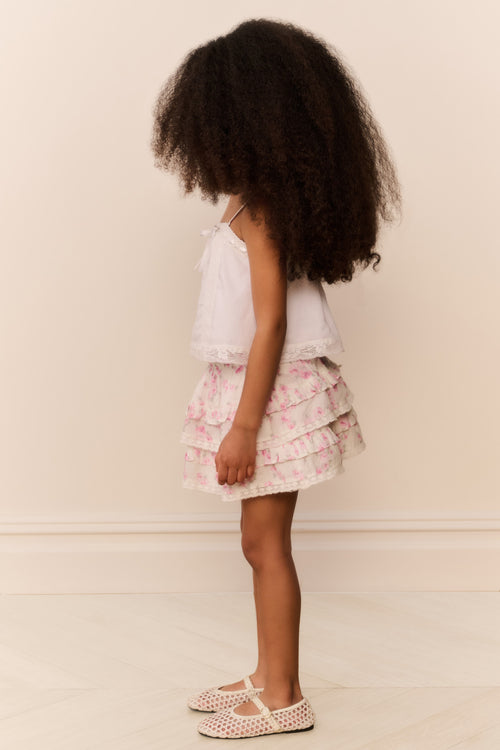 Young girl wearing a white top and floral ruffle skirt against a plain background