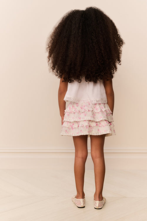 Young girl wearing a skirt dress with ruffled layers against a plain background