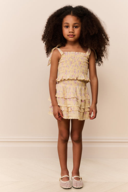 Young girl wearing a tiered yellow skirt with matching top with a neutral background