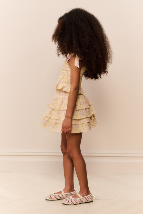 Young girl wearing a tiered yellow skirt with matching top with a neutral background