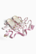 Two white floral shoes with decorative ribbons on a white background
