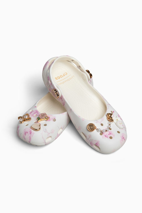 Pair of white shoes with floral and gold charms on a white background