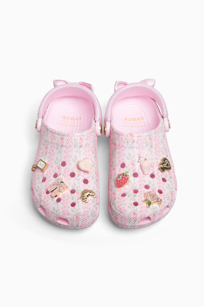 Pink rubber clogs with decorative charms on a white background