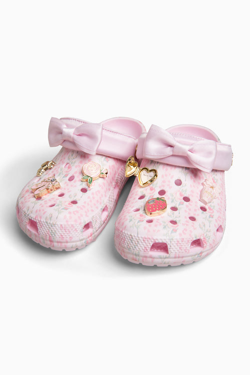 Pink croc shoes with bows and decorative elements on a white background