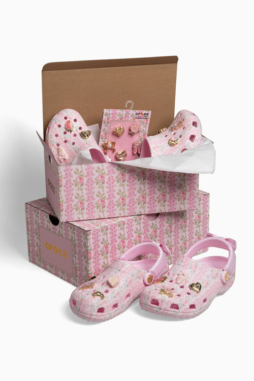 Pink children's shoes with gold hearts in a floral-patterned box on a white background