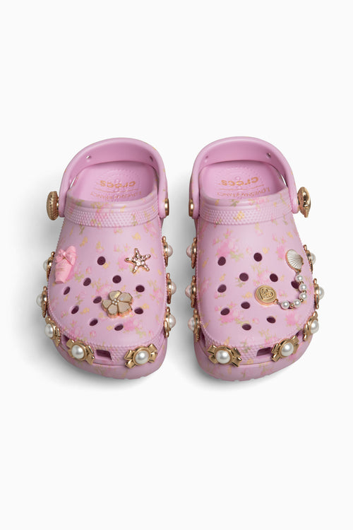 Pink croc clogs with decorative embellishments on a white background