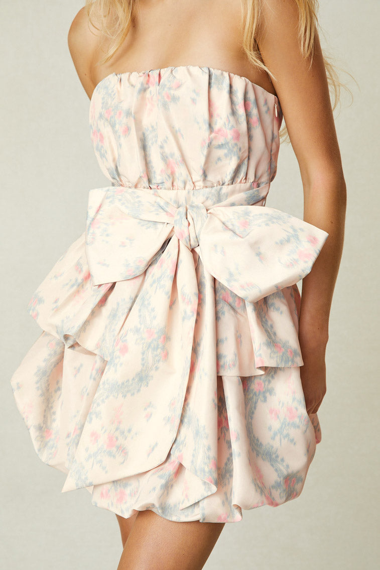 Model wearing light pink floral strapless mini dress with bow detail at waist