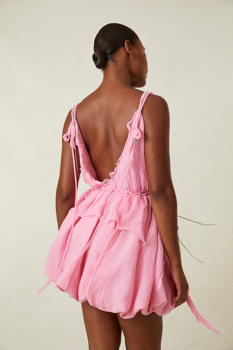 Side image of model wearing pink mini dress drapes and crystals at neckline and waist.