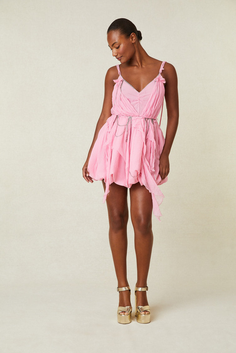 Model wearing pink mini dress drapes and crytals at neckline and waist.
