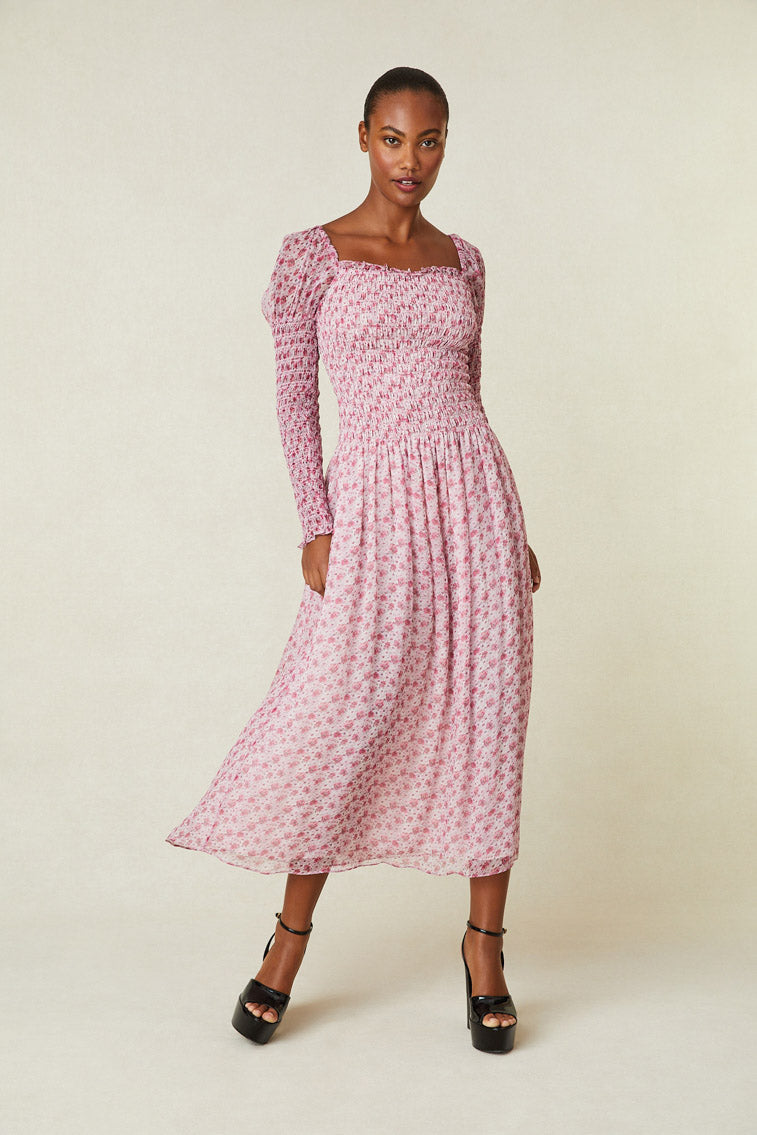 Model wearing pink floral maxi dress with smocked top, puffed shoulders, and an a-line skirt. 