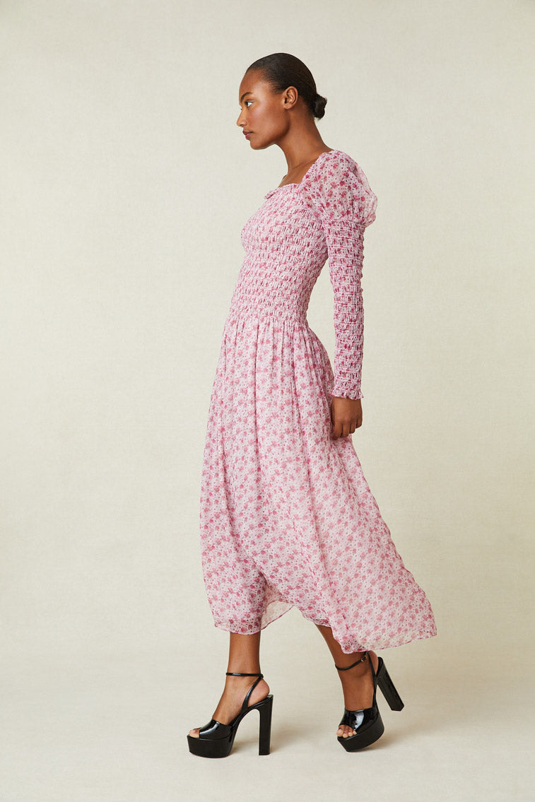 Side image of model wearing pink floral maxi dress with smocked top, puffed shoulders, and an a-line skirt.