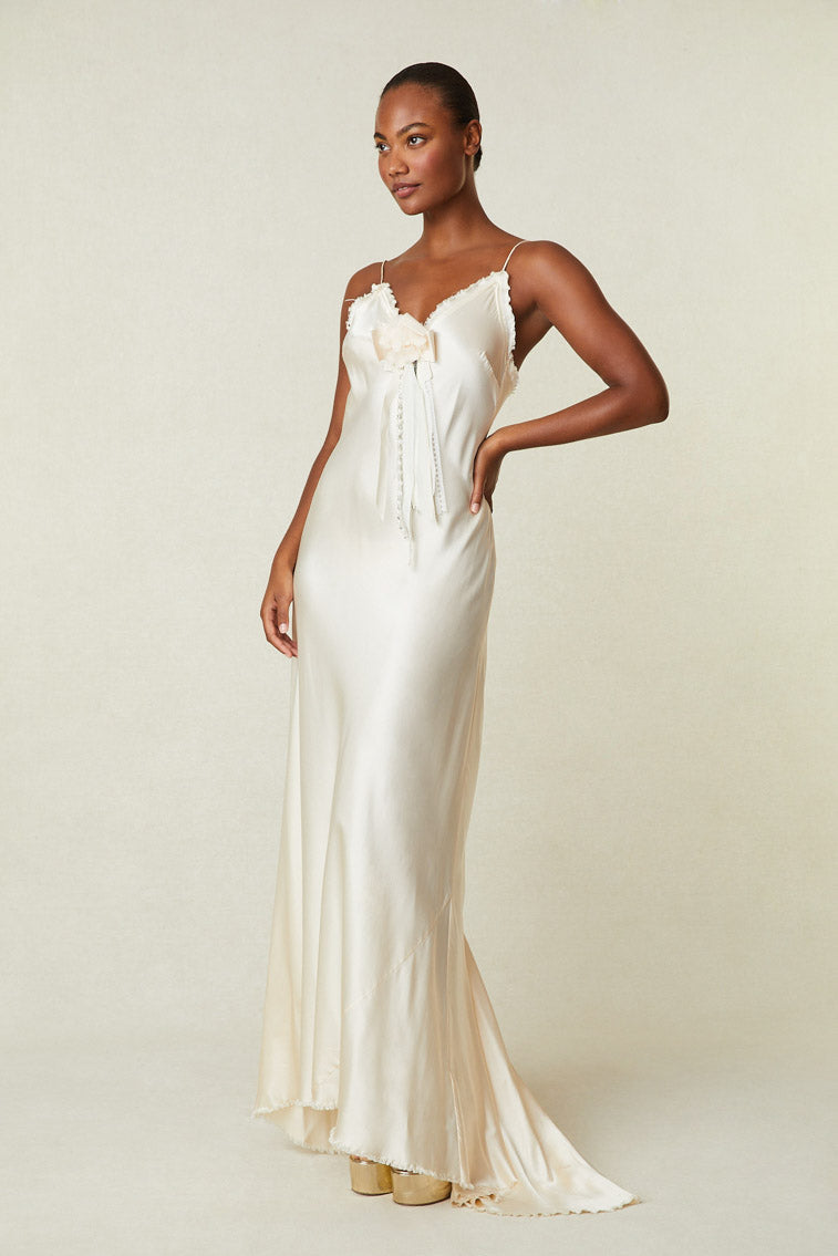 Model wearing cream silk maxi slip dress with removable rosette pin and raw hem