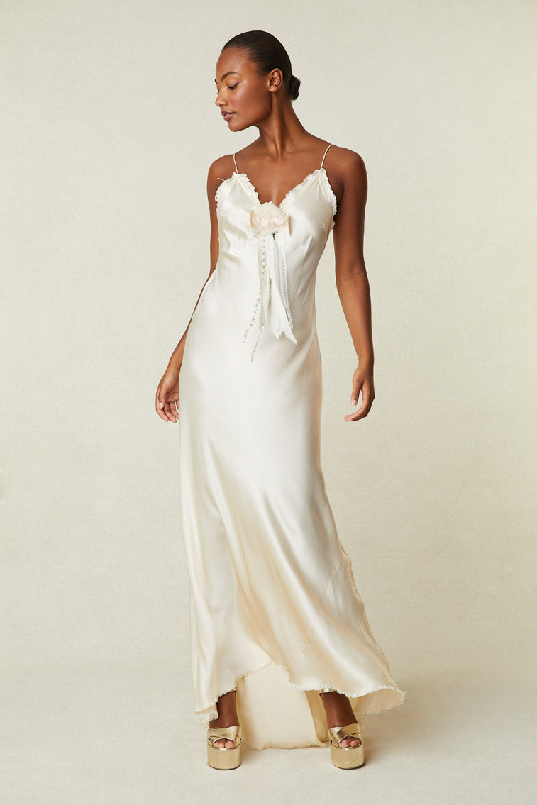 Model wearing cream silk maxi slip dress with removable rosette pin and raw hem