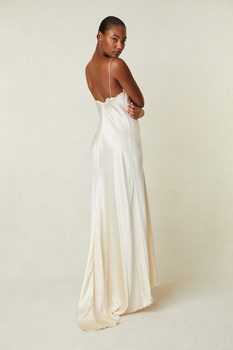 Back image of model wearing cream silk maxi slip dress with low back and raw hem