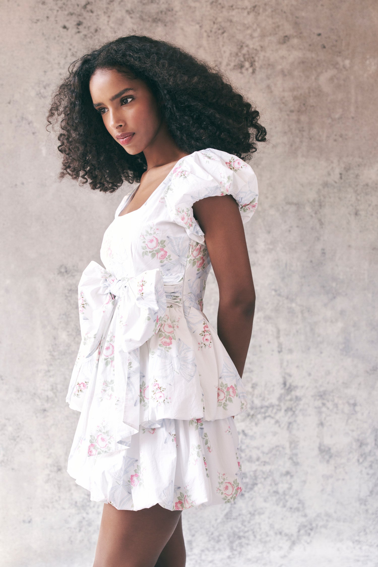 Side image of model wearing white floral babydoll mini dress