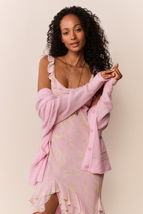 Woman wearing a pink dress with a matching cardigan against a beige background