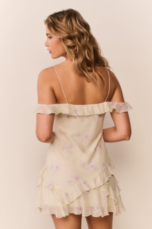 Woman wearing a light-colored off the shoulder dress with floral patterns on a plain background