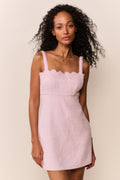 Woman wearing a pink dress with thin straps and scalloped neckline against a beige background