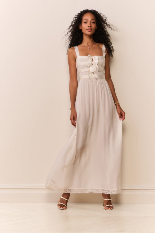 Woman wearing a white dress with bow details against a plain background