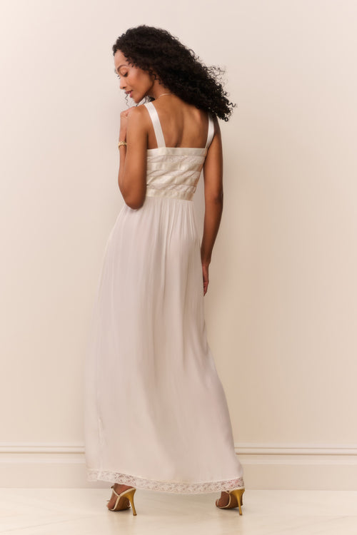 Woman wearing a white dress with bow details against a plain background