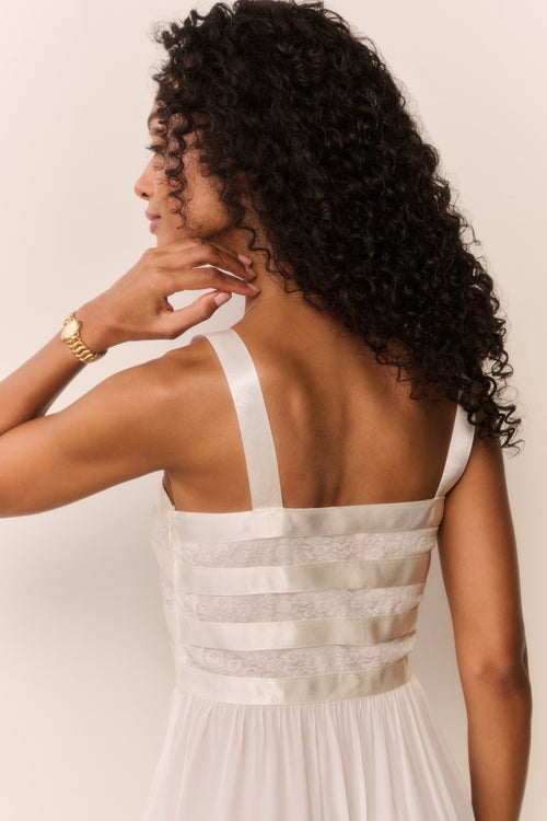 Woman wearing a white dress with thin straps, standing against a plain background