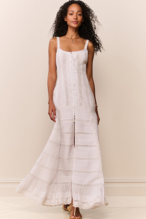 Woman wearing a white sleeveless top and lace maxi dress against a beige background