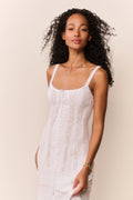 Woman wearing a white sleeveless top and lace maxi dress against a beige background