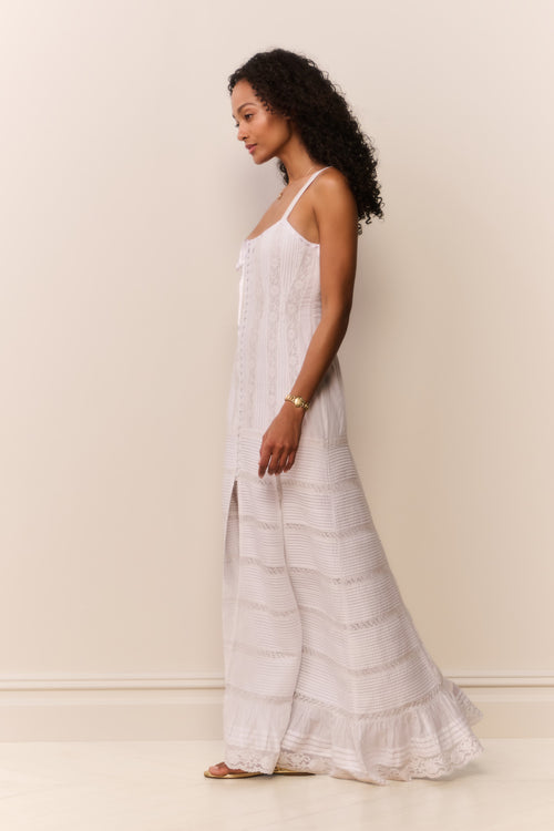 Woman wearing a white sleeveless top and lace maxi dress against a beige background