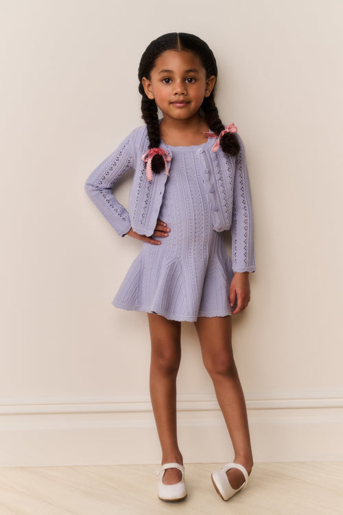 Young girl wearing a light blue cardigan and dress outfit against a plain background
