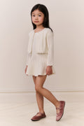Young girl wearing a cream-colored knit cardigan and skirt outfit against a plain background