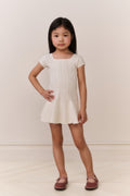 Young girl wearing a white knit dress standing against a plain background