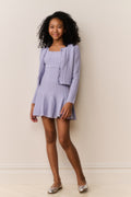 Young girl wearing a light purple dress and matching cardigan against a plain background