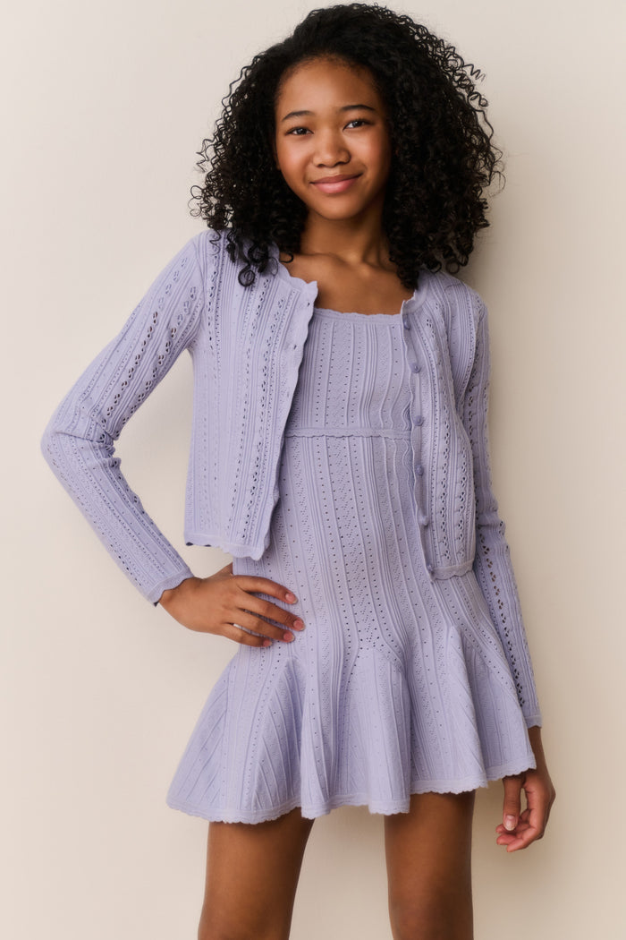 Young girl wearing a light purple dress and jacket against a plain background