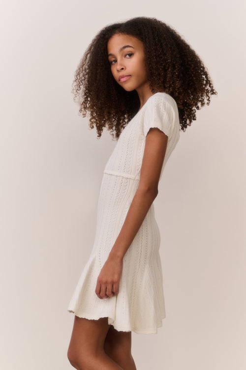 Tween wearing a white knit dress with a plain background