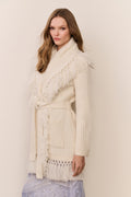 Woman wearing a cream-colored fringed sweater against a plain background
