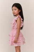 Young girl wearing a pink ruffled dress against a plain background