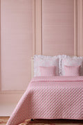 Pink quilted bedspread and pillows on a bed against a pink paneled wall.