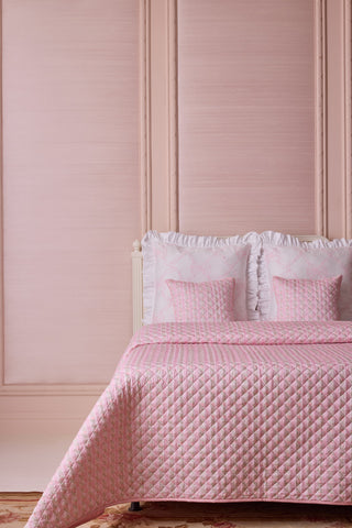 Pink quilted bedspread and pillows on a bed against a pink paneled wall.