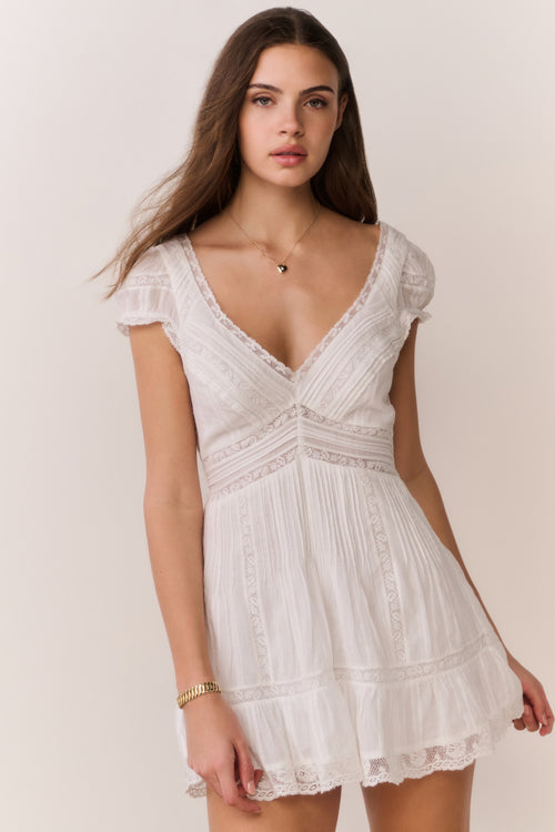 Woman wearing a white lace dress with a heart-shaped necklace against a plain background