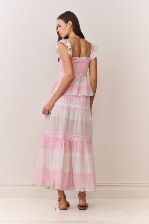 Woman wearing a pink and white ruffle top and matching skirt with a plain background