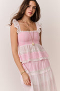 Woman wearing a pink ruffle top with lace details and matching skirt on a plain background