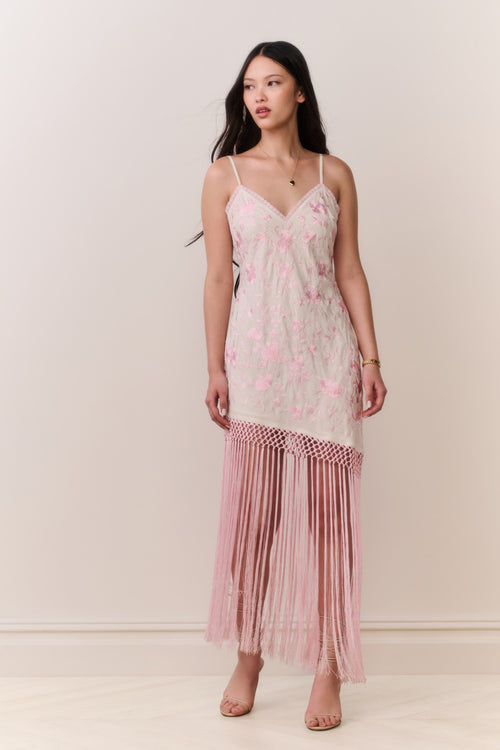 Woman wearing a pink floral dress with fringe hemline details on a plain background