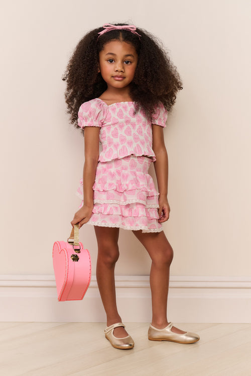 Young girl in a pink floral dress holding a pink handbag against a white wall