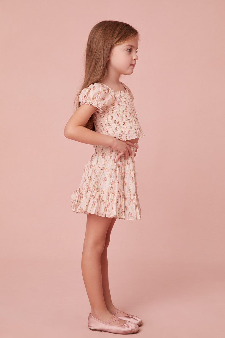 top features a dainty floral print, a smocked center front, short puff sleeves, and sweet ruffle detailing at the sleeve openings, neckline and the hem.