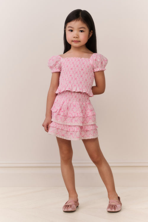 Young girl wearing a pink patterned ruffle top and matching skirt against a plain background
