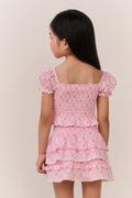 Young girl wearing a pink patterned ruffled top and matching skirt against a plain background