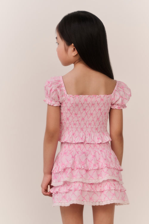 Young girl wearing a pink patterned ruffled top and matching skirt against a plain background