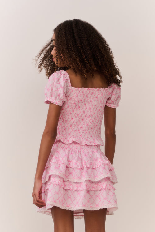 Young girl wearing a pink bow pattern top and matching ruffle skirt against a plain background